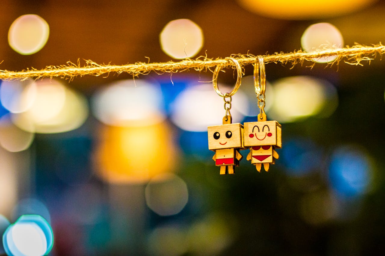 home-img Charming wooden cartoon keychain dolls hanging with vibrant bokeh lights in the background, creating a playful and colorful ambiance.